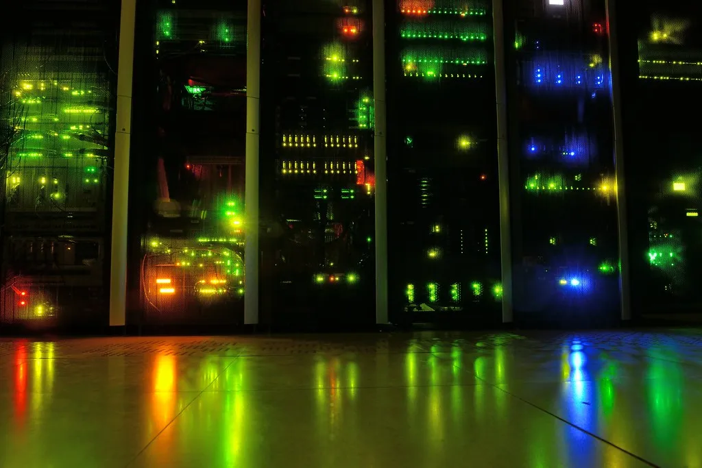 Server-room rack line at night — dense infrastructure lit only by status LEDs